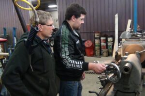 Martyn Novacek operating the turning lathe while mentor Doug Hlucny assists.